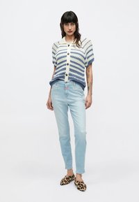 Πλεκτή ζακέτα με μπλε και κρεμ ρίγες, κοντά μανίκια και κουμπιά στο μπροστινό μέρος. Συνδυάζεται με ανοιχτό μπλε τζιν παντελόνι και παπούτσια με λεοπάρ σχέδιο.