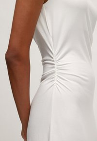 Witte jurk met zijruching die textuur creëert. Een gladde, rekbare stof met een aansluitende silhoutte bij de taille.