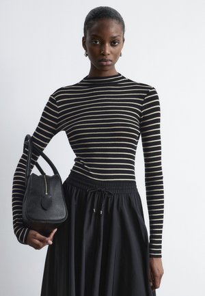 Striped long-sleeve top in black and beige paired with a black, casual skirt. Holding a small black handbag with a zipper and rounded edge.