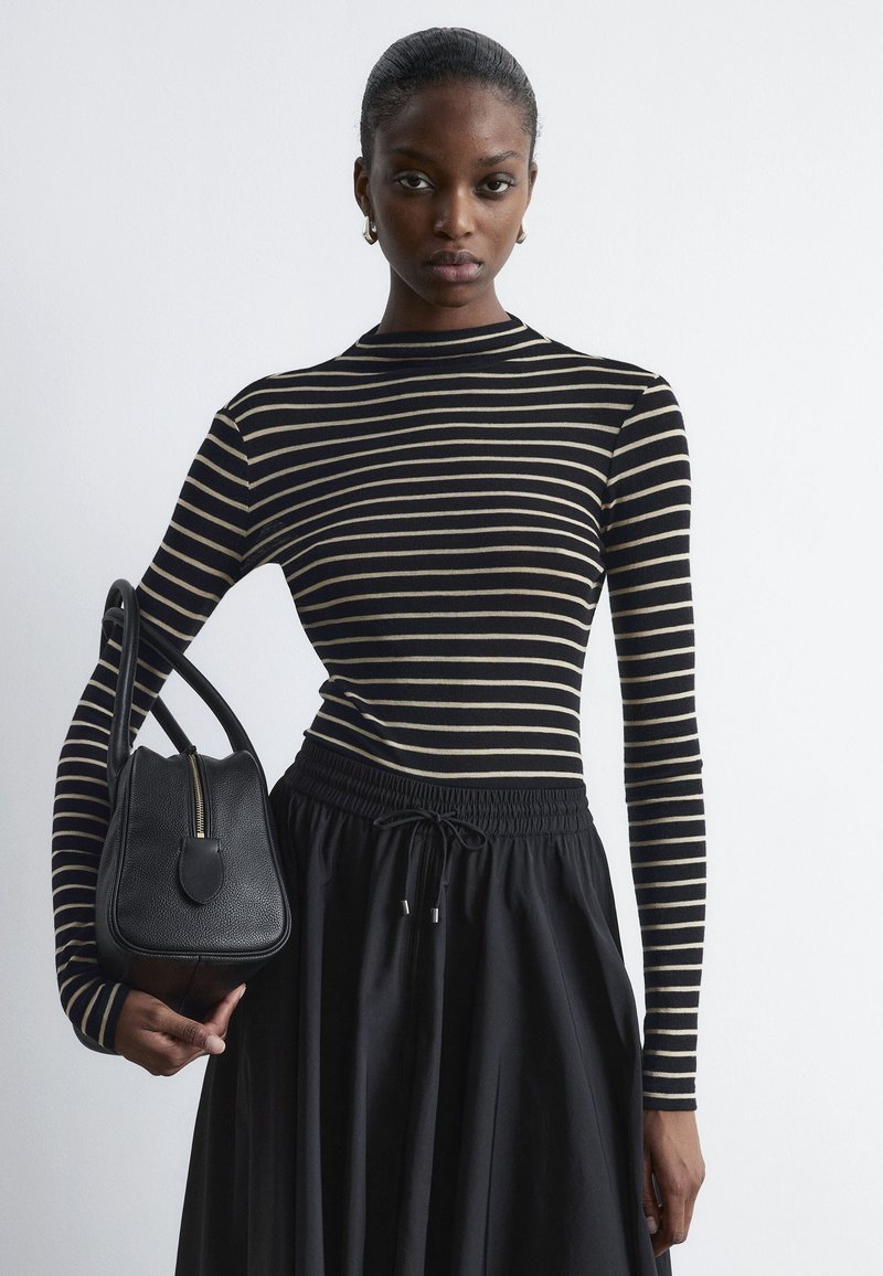 Gestreiftes Langarmoberteil in Schwarz und Beige, kombiniert mit einem schwarzen, lässigen Rock. Hält eine kleine schwarze Handtasche mit Reißverschluss und abgerundeten Kanten.