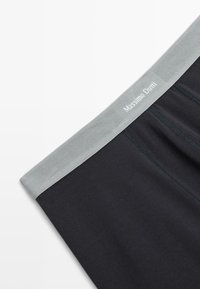 Černé boxerky z elastického materiálu s šedým elastickým pasem, včetně decentního loga značky uprostřed a hladkého povrchu.