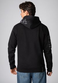 Zwarte hoodie met een kangoeroezak, gestructureerde stof en een capuchon met grijze tekst. Lange mouwen en ribgebreide manchetten maken het ontwerp compleet.