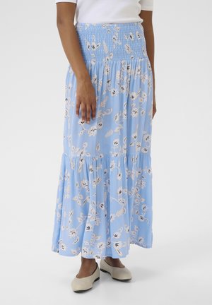 Jupe maxi bleue à fleurs avec une taille smockée, un design en couches et un tissu fluide. Présente des motifs floraux crème et noirs. Assortie à des chaussures beiges.