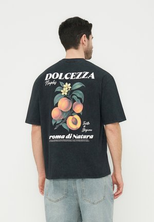 Άνδρας βλέποντας προς τα πίσω, φοράει μαύρο μπλουζάκι με ροδάκινα, λουλούδια και λευκό κείμενο που γράφει "DOLCEZZA Naples" και "aroma di Natura."