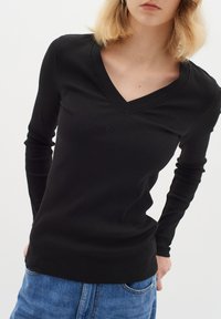 Top nero a maniche lunghe con scollatura a V, tessuto a coste, design aderente e cuciture curate, abbinato a jeans blu.