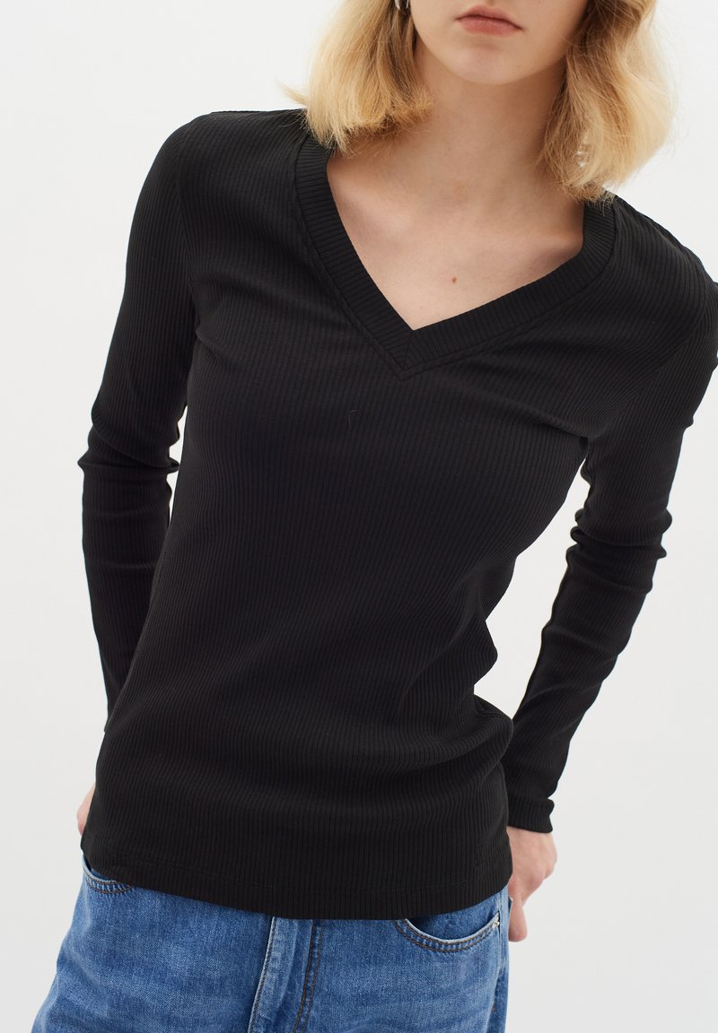 Top nero a maniche lunghe con scollatura a V, tessuto a coste, design aderente e cuciture curate, abbinato a jeans blu.