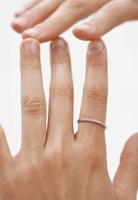 Anillo de plata con pequeñas piedras preciosas transparentes, colocado en un dedo con textura de piel natural. La luz se refleja en las gemas, enfatizando su claridad.