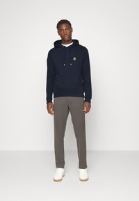 Tums zils kapucis ar kanga rācijas kabatu un novilkšanas kapuci, ar zelta logo. Nēsāts ar pelēkiem biksēm un baltām sporta apaviem.