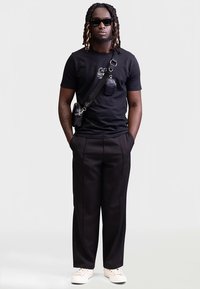 Melna T-krekls ar baltu tekstu, melnas bikses un baltas sporta kurpes. Aksesuāri: maza melna soma un saulesbrilles. Vienkāršs dizains.