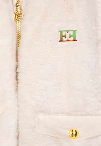 Giacca zip-up in pile crema con hardware dorato, caratterizzata da un logo ricamato "EH". Include una tasca con bottone sul fondo.
