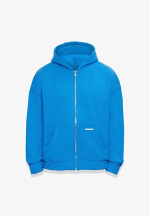 Zila kapuca džemperis, izgatavots no mīksta kokvilnas maisījuma auduma, ar kapuci, priekšējām kabatām un ribotiem piedurknēm. Nav novērojamas rakstu vai akcenti.