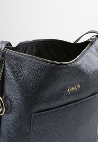 Navy blue leather handbag with a textured finish, featuring a front pocket, gold hardware, and a zippered top closure.