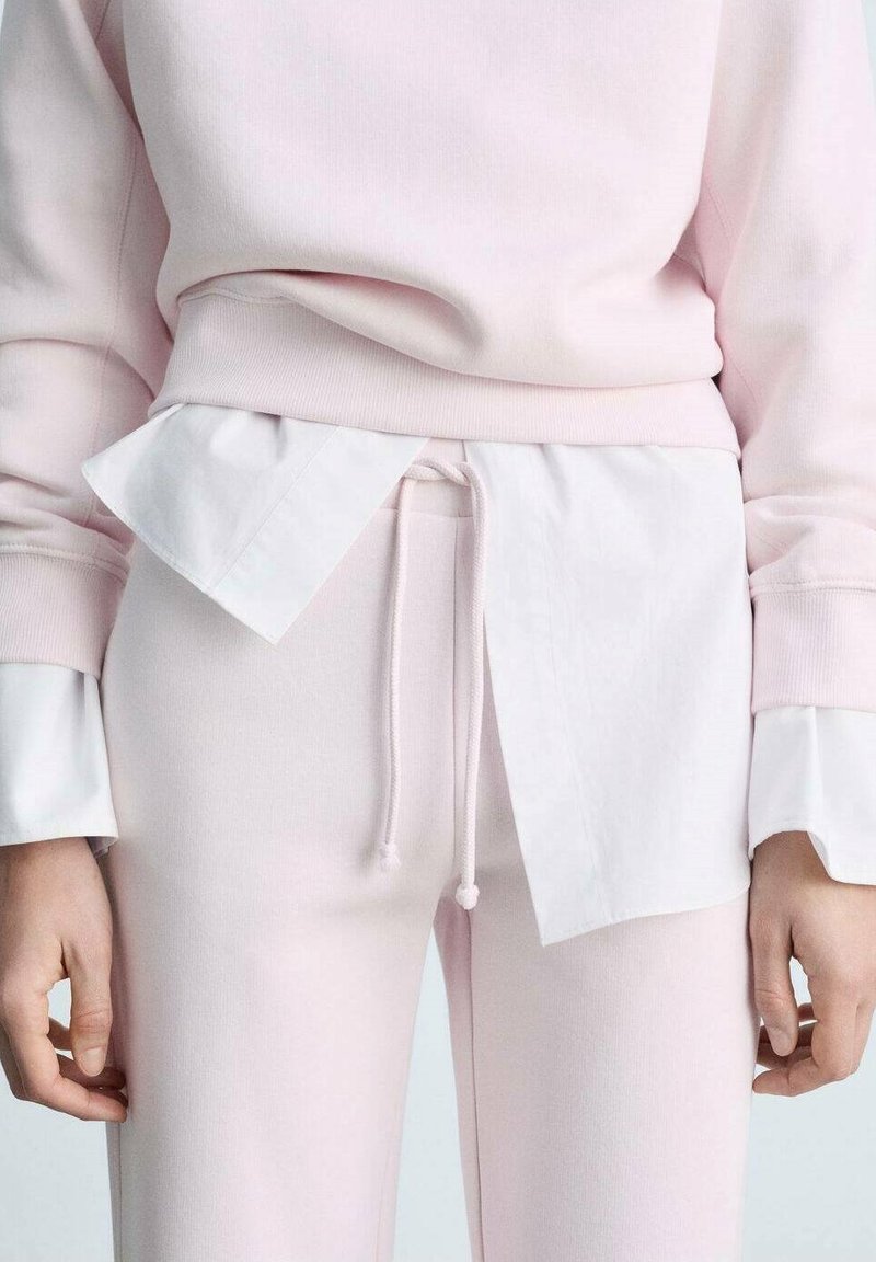 Ljusrosa sweatshirt med ribbat mönster och vit lagerpanel vid midjan. Matchande ljusrosa joggers med dragsko i midjan.
