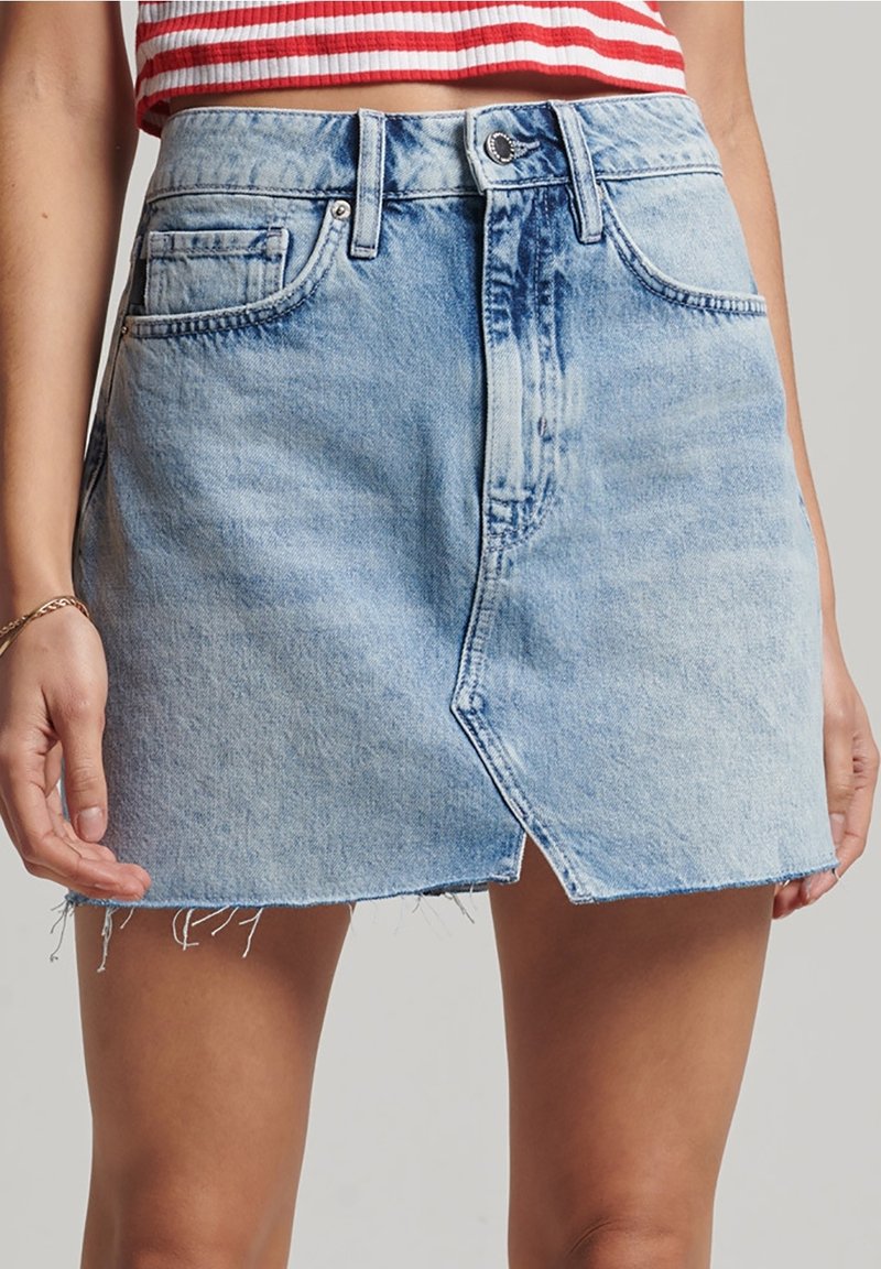 Lichtblauwe denimrok met een voorknos, een rafelige zoom en een klassieke vijf-pocket ontwerping. Voorzien van een knoopsluiting en riemlussen.
