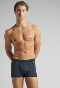 Ropa interior estilo bóxer de color azul marino con una textura suave, una cinturilla en contraste y un detalle de bolsa frontal. Presencia mínima de marca.
