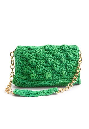 Sac à main vert crocheté avec un motif texturé à boules et une bandoulière chaîne dorée avec un coussinet crocheté.