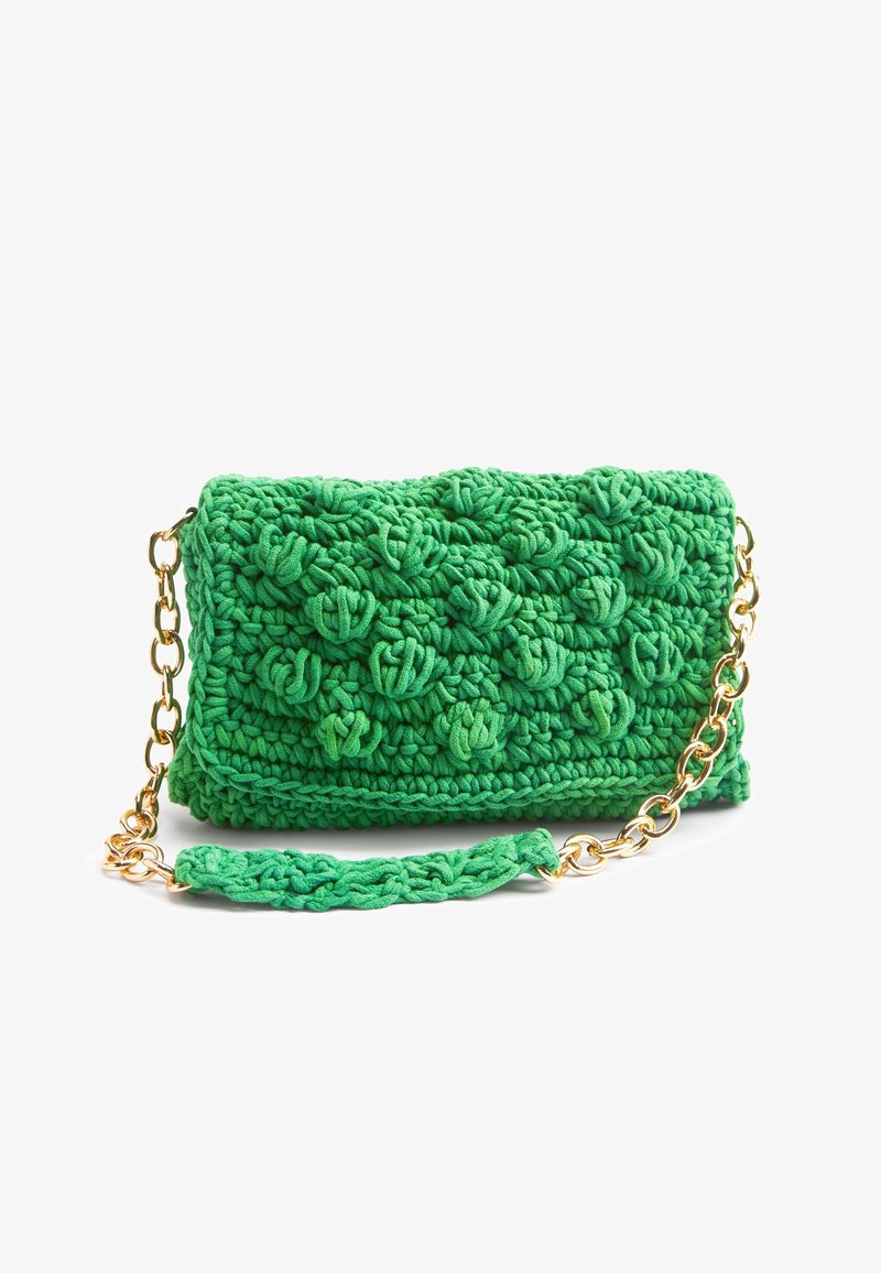 Sac à main vert crocheté avec un motif texturé à boules et une bandoulière chaîne dorée avec un coussinet crocheté.