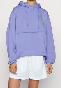 Violetti lyhyt huppari pehmeästä kankaasta, jossa on etutasku, nyörit ja vaaleanvihreät yksityiskohdat. Yhdistetty valkoisiin shortseihin.