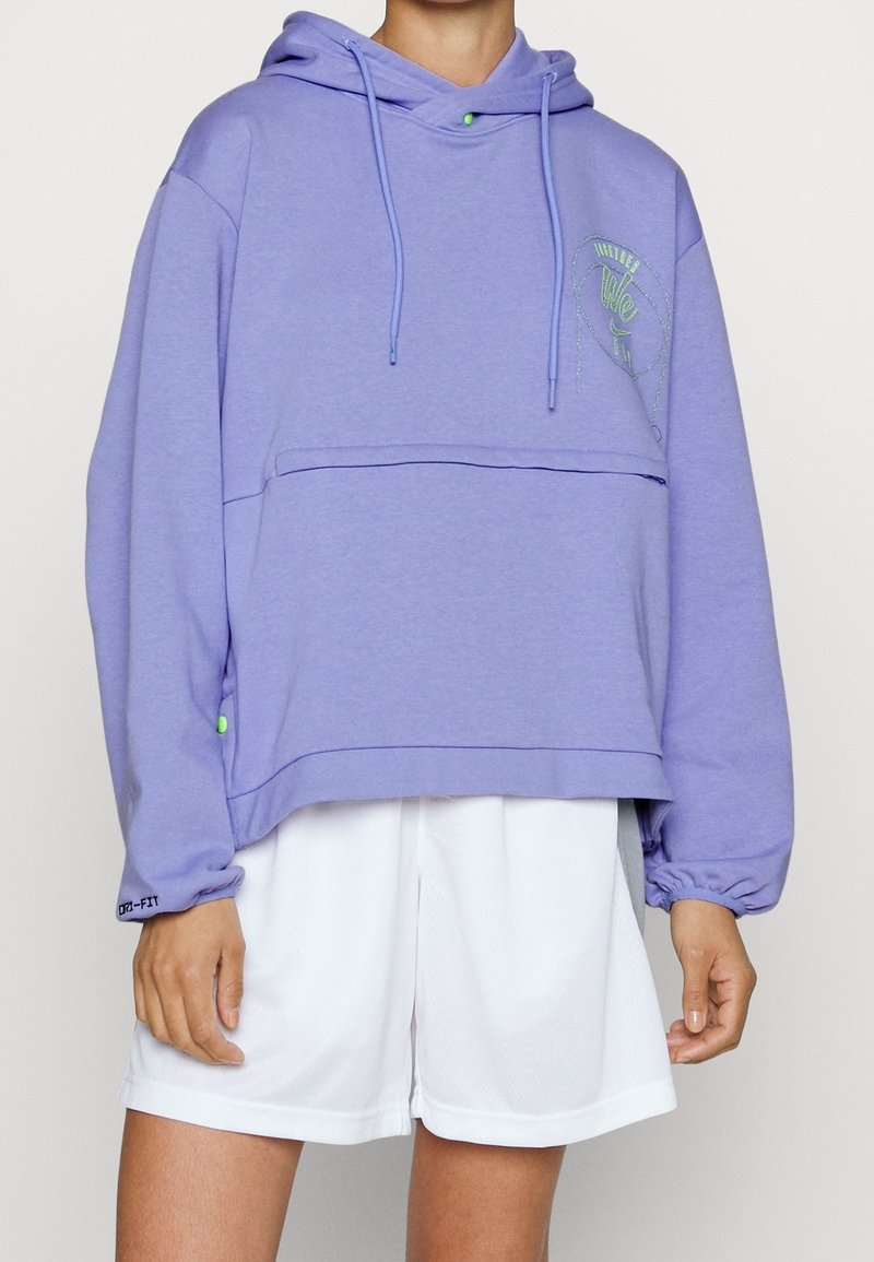 Violetti lyhyt huppari pehmeästä kankaasta, jossa on etutasku, nyörit ja vaaleanvihreät yksityiskohdat. Yhdistetty valkoisiin shortseihin.