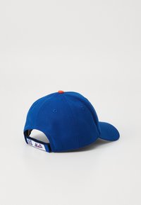 Kék baseball sapka lekerekített koronával, egyenes napellátóval és piros felső gombbal. Állítható pánttal rendelkezik, valamint egy logóval ellátott folttal a hátsó részén.