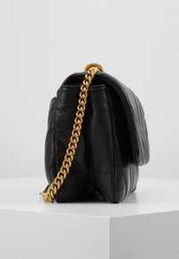 Czarna skórzana torebka z pikowanym wzorem, wyposażona w złoty łańcuszkowy pasek i usztywniony kształt. Torebka ma gładką fakturę oraz górną klapę.