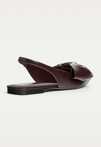 Dark brown leather flat slingback shoe with pointed toe and large folded bow detail on top, shown against a white background.