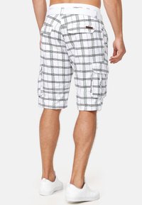 Shorts cargo à carreaux blancs avec des lignes vertes ; dotés de poches latérales et d'une ceinture confortable, présentés de dos. Baskets blanches visibles.