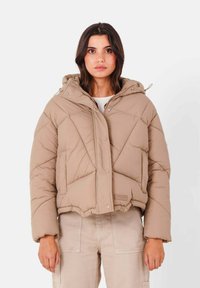 Giubbotto imbottito beige con cappuccio, caratterizzato da un design trapuntato, bottoni a scatto e un taglio corto. Il materiale appare morbido con una finitura opaca.