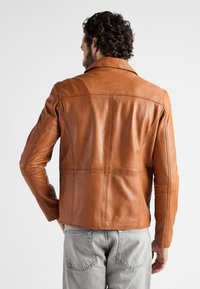 Brun læderjakke med klassisk krave, skræddersyet pasform og detaljeret syning, parret med lysegrå jeans.