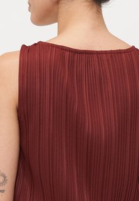 Haut sans manches bordeaux avec des plis verticaux, texture douce et encolure ronde. Montre la vue arrière avec des détails de couture lisses.