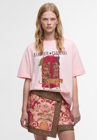 Φωτεινό ροζ oversized t-shirt με γραφικό ενός κόκκινου τηλεφωνικού θαλάμου, μαζί με μια λεοπάρδαλη και τροπικά στοιχεία. Συνδυάζεται με μια κοντή φούστα με λουλουδάτη κέντημα.