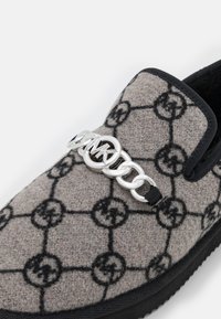 Gros plan sur une chaussure en tissu gris à enfiler avec un motif géométrique noir et un détail en chaîne argentée comportant les lettres M et K sur la tige.