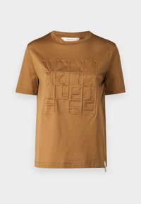 T-shirt di cotone marrone con colletto rotondo, caratterizzato da una grafica testurizzata in rilievo, disposta in una formazione quadrata sulla parte anteriore. Maniche corte.