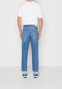 Modré denimové džíny s volným střihem, mají rovné nohavice a dvě zadní kapsy. Nosené s bílou košilí s krátkým rukávem a teniskami.