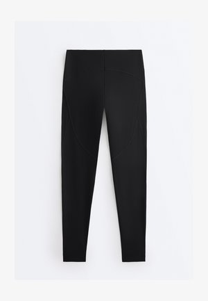 Svarte leggings med høj talje og synlige sømdetaljer, vist fladt mod en enkel hvid baggrund.