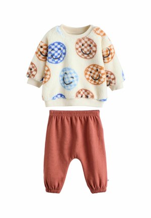 Cremfarbener Fleece-Kindersweatshirt mit bunten Smiley-Gesichtern und rostfarbener Hose mit elastischem Bund und gerafften Bündchen.