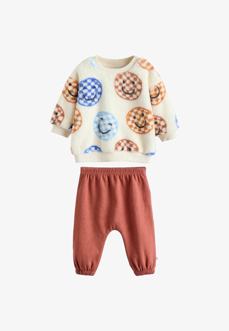 Cremfarbener Fleece-Kindersweatshirt mit bunten Smiley-Gesichtern und rostfarbener Hose mit elastischem Bund und gerafften Bündchen.