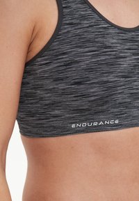 Musta urheiluliivimalli, jossa on teksturoitu, heather-kuvio, sileät reunat ja valkoinen "ENDURANCE"-logo vyötäröllä.