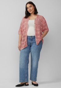 Losjes gebreide, rood-witte cardigan met korte mouwen, gedragen over een witte top, gecombineerd met lichtblauwe, high-waisted jeans en zwarte ballet flats.