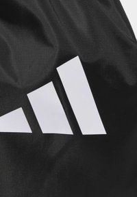 Black fabric with a textured surface features prominent white Adidas three-stripe logo in geometric design.