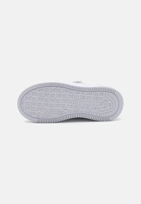 Semelle de sneaker blanche avec caoutchouc texturé, motifs circulaires, et un logo de marque. Comprend des bords surélevés et un talon courbé pour une meilleure adhérence.