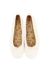 Zapatillas blancas planas con punta redondeada y un detalle de lazo. El interior presenta un patrón de estrellas multicolores sobre un fondo marrón claro.