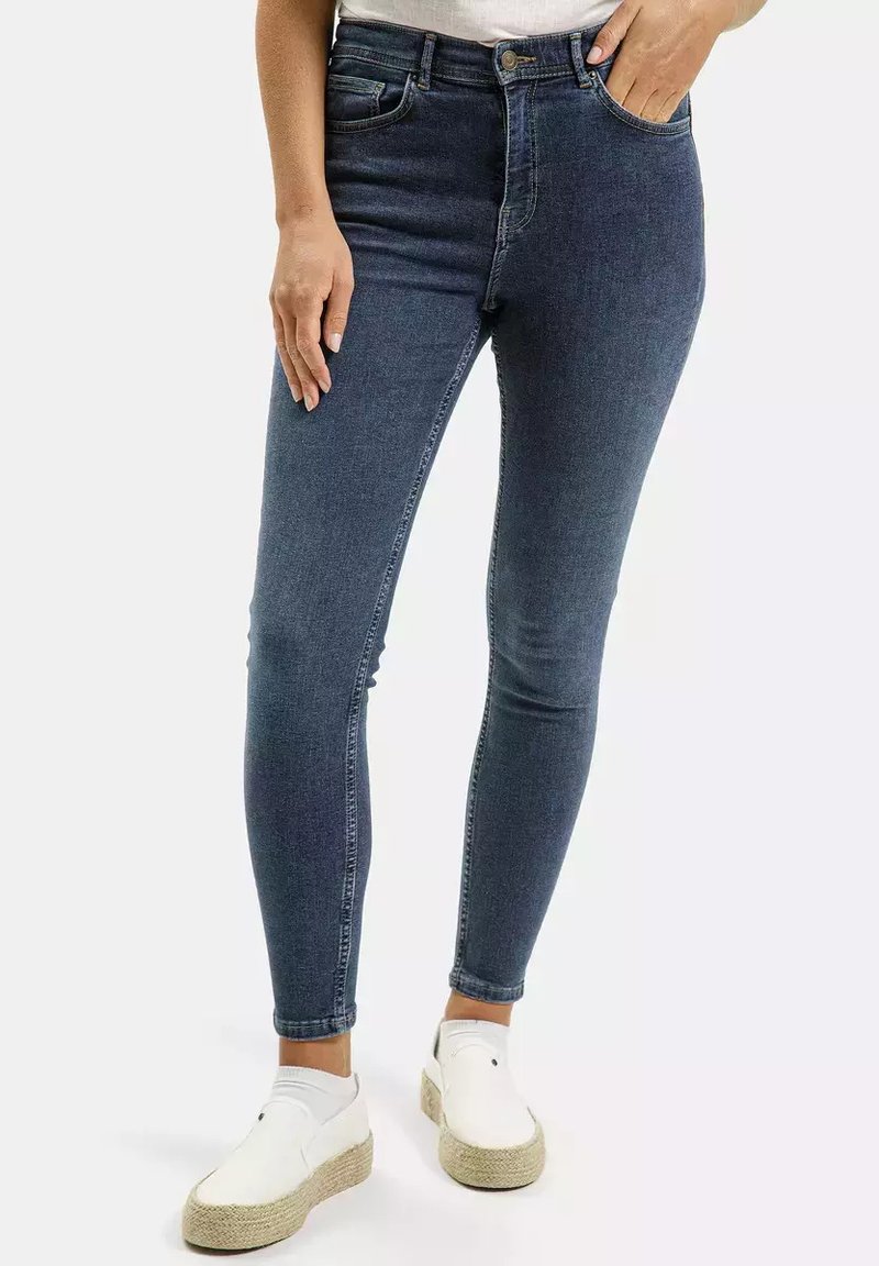 Ciemnoniebieskie rurki z denimu, posiadające wysoki stan, kieszenie z przodu i gładką teksturę. Noszone z białymi butami w stylu espadryli.