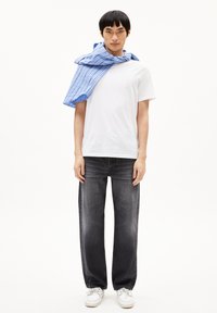 Witte t-shirt, donkergrijze wijde jeans en witte schoenen. Een blauw gestreept shirt is om de schouders gedrapeerd. Eenvoudig en Casual ontwerp.