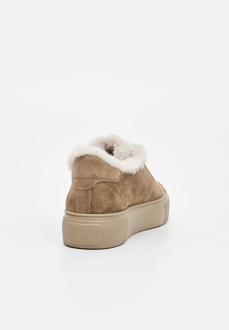 Braune Wildledersneaker mit einem cremefarbenen Kunstfellfutter, gepolstertem Kragen und einer dicken beigefarbenen Gummisohle. Er hat eine abgerundete Zehenpartie und minimale Details.