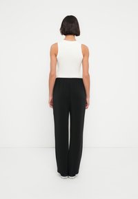 Λευκό αμάνικο τοπ συνδυασμένο με μαύρο παντελόνι ψηλής μέσης. Το σύνολο έχει χαλαρή σιλουέτα και ομαλή υφή.