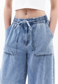 Vaaleansiniset farkkuista valmistetut leveälahkeiset housut, joissa on joustava vyötärö ja nyöri, kaksi etutaskua ja rento istuvuus.