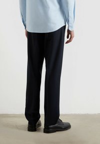 Jasnoniebieska koszula z długimi rękawami, w zestawieniu z ciemnymi spodniami i czarnymi butami. Koszula ma zaokrąglony dół i gładką teksturę.