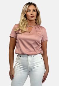 Blush pink short-sleeve blouse with a V-neck and pleat details, paired with white high-waisted jeans, smooth fabric, minimal accents.
