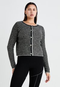 Svart och vit texturerad cardigan med rund halsringning, knäppning framtill och kontrasterande kant. Långa ärmar, kort design och dekorativa knappar.